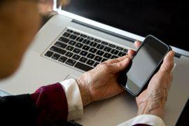 A man holding his phone in front of his laptop