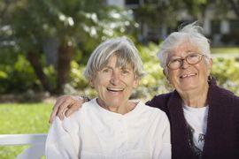 Two woman smiling on a bench outside sitting together