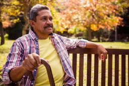 A man holding his cane sitting on a bench outside