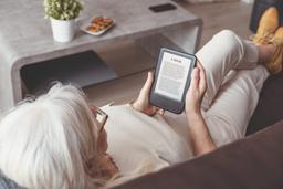 A woman sitting on her couch reading an e-book